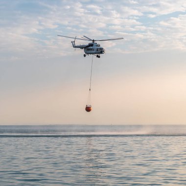 Bir yangın helikopter denize su toplar ve orman yangını söndürmek için dağlara doğru uçar.