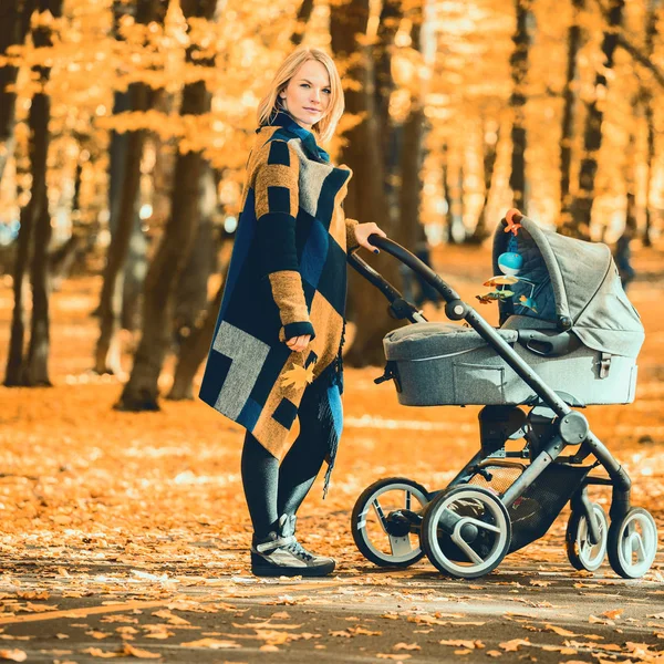 Una joven madre con un cochecito pasea por el parque de otoño — Foto de Stock