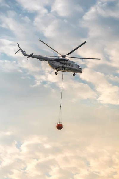 Een brandweerman helicopter met een volledige korf van water vliegt tegen een mooie hemel — Stockfoto