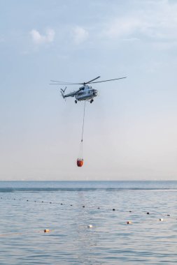Bir helikopter kırmızı bir sepet ile denizin üzerinde su yakalamak için indirilir.