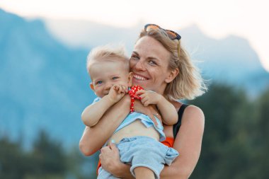 Genç küçük oğlu onun kollarında tutan anne ve dağ manzarası fonunda oynanır