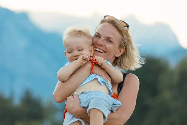 Jeune mère tenant son petit fils dans ses bras et ils sont joués dans le contexte d'un paysage de montagne — Photo