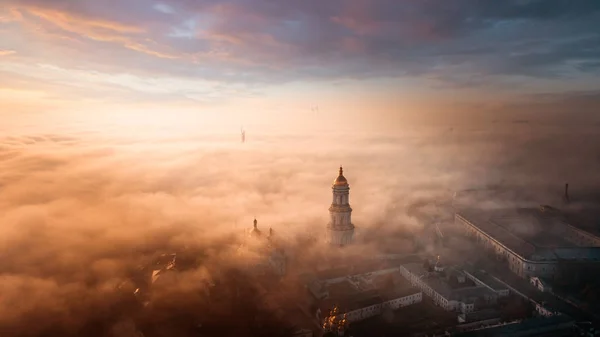 Letecký pohled Kyjevskopečerská lávra za úsvitu a město pokryté hustou mlhou v pozadí. — Stock fotografie