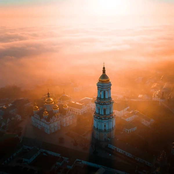 Letecký pohled Kyjevskopečerská lávra za úsvitu a město pokryté hustou mlhou v pozadí. — Stock fotografie