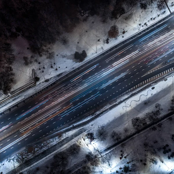 Top down view to night road with passing cars with headlights on between the winter park — Stock Photo, Image