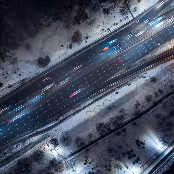 Top down view to night road with passing cars with headlights on between the winter park — Stock Photo, Image