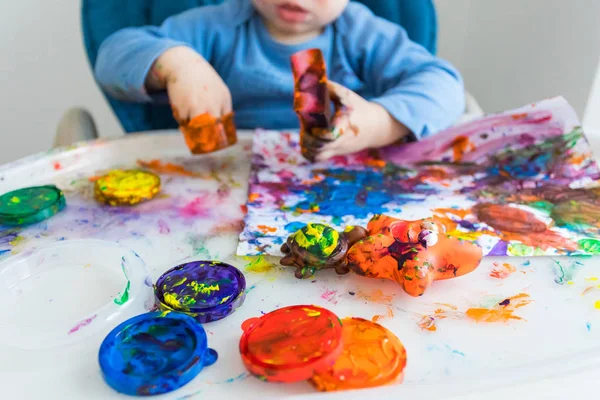 Ребенок рисует пальцами на бумаге за детским столом — стоковое фото