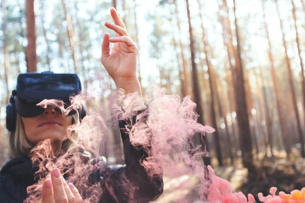 A woman wearing virtual reality goggles in the forest sees smoke bombs. VR glasses.