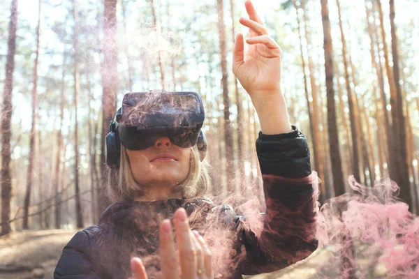 A woman wearing virtual reality goggles in the forest sees smoke bombs. VR glasses.