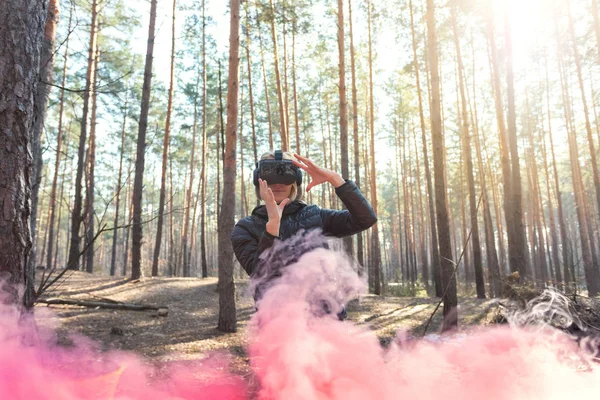 Uma mulher usando óculos de realidade virtual na floresta vê bombas de fumaça. óculos VR . — Fotografia de Stock