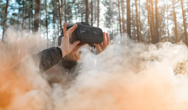 Woman in forest with virtual reality headset looking straight with orange smoke from smoke bombs