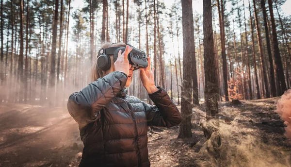 Woman in forest with virtual reality headset looking straight with orange smoke from smoke bombs