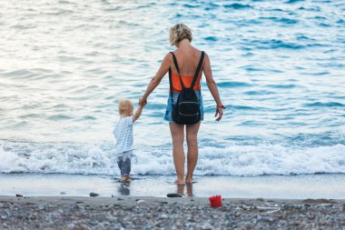 Anne ve oğlu gün batımında sahilde yürüyor.