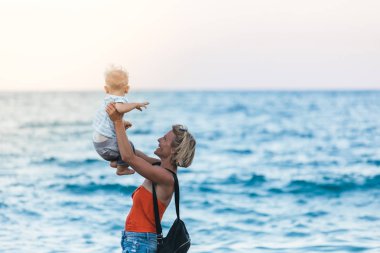 Anne ve oğlu gün batımında sahilde yürüyor.