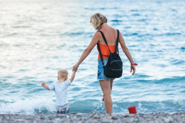 Anne ve oğlu gün batımında sahilde yürüyor.
