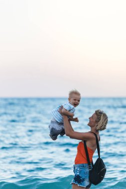 Anne ve oğlu gün batımında sahilde yürüyor.