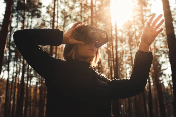 Woman in forest with virtual reality headset looking straight and trying to touch something with her hand