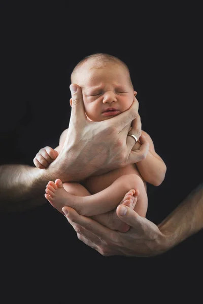 Vader houdt baby jongen op zijn handen tegen donkere achtergrond — Stockfoto