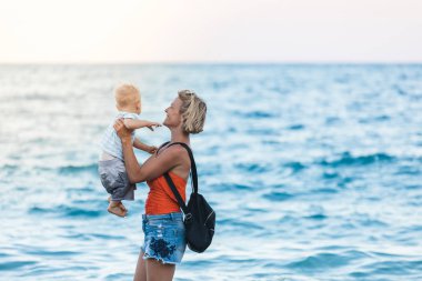 Anne ve oğlu gün batımında sahilde yürüyor.