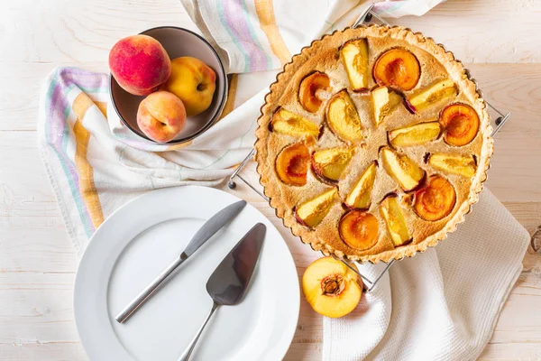 Homemade open peach pie on a white wooden background.