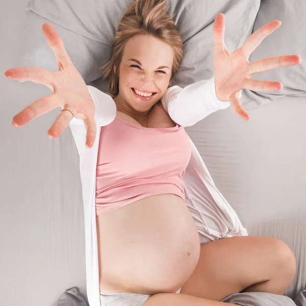 Счастливая беременная женщина лежит в постели и растягивается. Вид сверху — стоковое фото