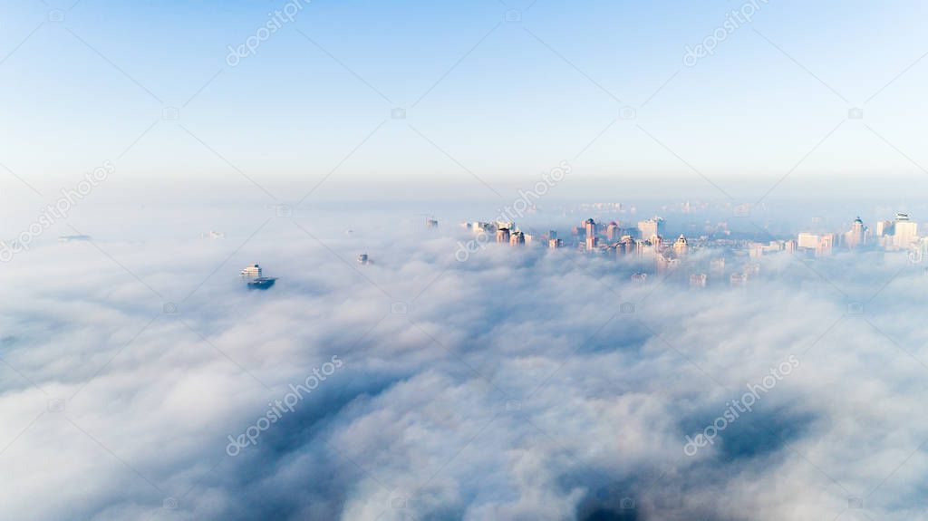 The city is covered with thick fog and protruding from it where neither where high-rise buildings