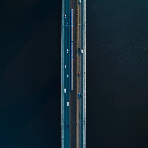 Brug met twee rijstroken en metro-of treinrails op een achtergrond van donker water. Luchtfoto — Stockfoto