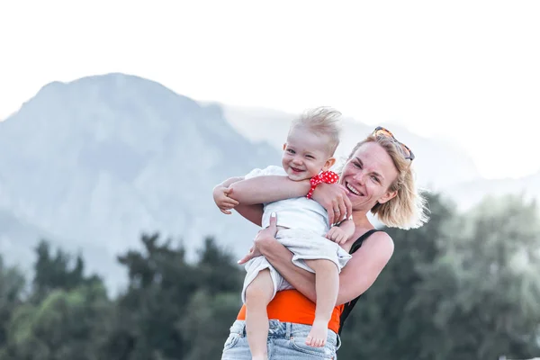 Jeune mère tenant son petit fils dans ses bras et lui montre quelque chose avec sa main au loin dans le contexte d'un paysage de montagne — Photo