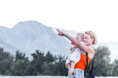 Genç küçük oğlu onun kollarında tutan anne ve onu eliyle bir şey bir dağ manzarası zemin karşı mesafe gösterir