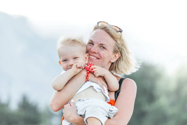 Jeune mère tenant son petit fils dans ses bras et ils sont joués dans le contexte d'un paysage de montagne — Photo