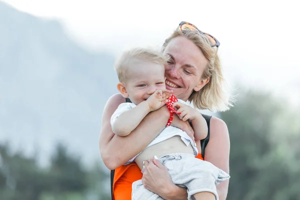 Jeune mère tenant son petit fils dans ses bras et ils sont joués dans le contexte d'un paysage de montagne — Photo