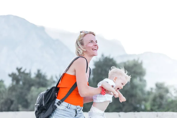 Jeune mère tenant son petit fils dans ses bras et ils sont joués dans le contexte d'un paysage de montagne — Photo