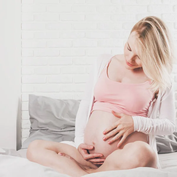 Felice giovane donna incinta si trova a letto e accarezza la pancia . — Foto Stock