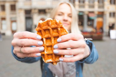 Brüksel'deki Büyük Pazar Meydanı'nın arka planında geleneksel Belçika waffle'ı tutan genç güzel kadın, Belçika