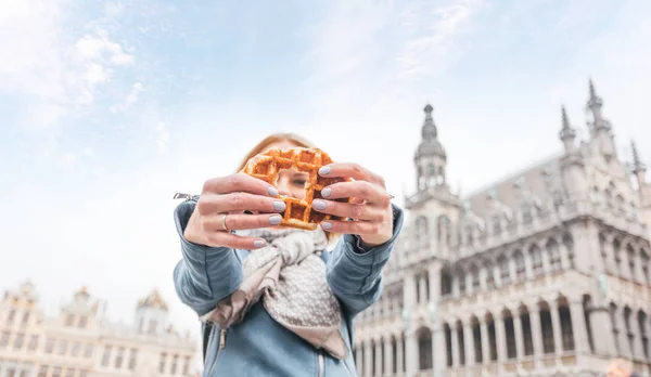 Jovem mulher bonita segurando um waffle belga tradicional no fundo da Grande Praça do Mercado em Bruxelas, Bélgica — Fotografia de Stock