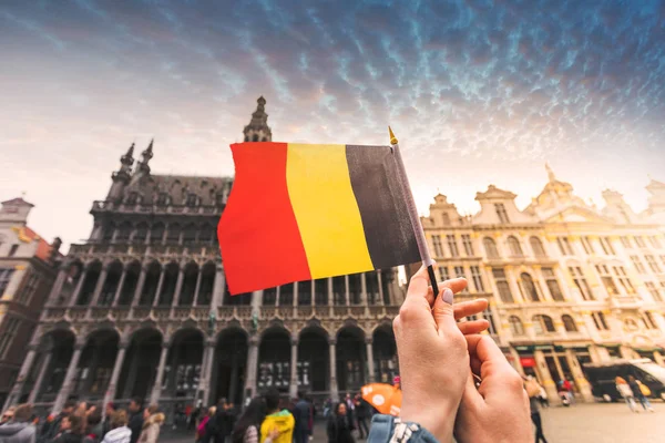 Woman tourist holds in her hand a flag of Belgium against the background of the Grand-Place Square in Brussels, Belgium