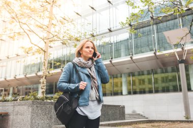 Ofis binaları arka planda, sokakta cep telefonuyla çalışan bir yönetici.