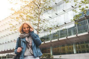 Ofis binaları arka planda, sokakta cep telefonuyla çalışan bir yönetici.