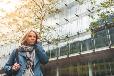Ofis binaları arka planda, sokakta cep telefonuyla çalışan bir yönetici.