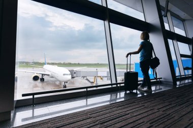 Havaalanında, pencereden uçaklara bakan genç bir kadın..