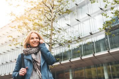Ofis binaları arka planda, sokakta cep telefonuyla çalışan bir yönetici.