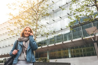 Ofis binaları arka planda, sokakta cep telefonuyla çalışan bir yönetici.