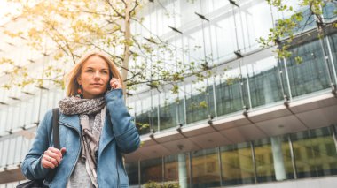 Ofis binaları arka planda, sokakta cep telefonuyla çalışan bir yönetici.