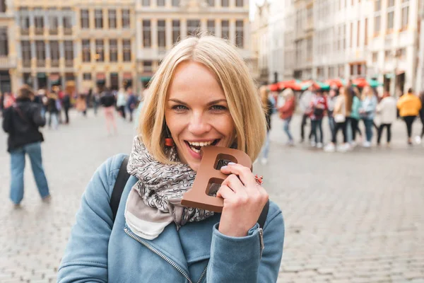 Woman tourist bites a bar of chocolate at the Grand Place in Brussels, Belgium — Stock Photo, Image