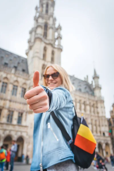 Joven mujer alegre feliz mostrando el pulgar hacia arriba contra el telón de fondo de la Grand Place en Bruselas, Bélgica — Foto de Stock