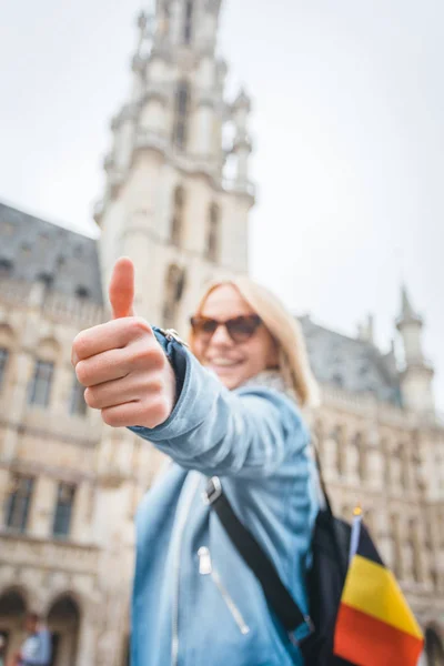 Jovem feliz mulher alegre mostrando polegar para cima contra o pano de fundo da Grand Place em Bruxelas, Bélgica — Fotografia de Stock