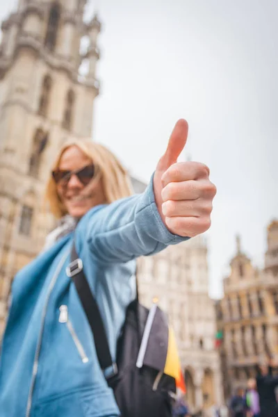 Joven mujer alegre feliz mostrando el pulgar hacia arriba contra el telón de fondo de la Grand Place en Bruselas, Bélgica — Foto de Stock