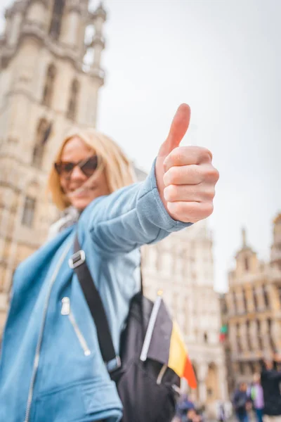 在比利时布鲁塞尔大广场的背景下,年轻快乐开朗的女人竖起大拇指 — 图库照片