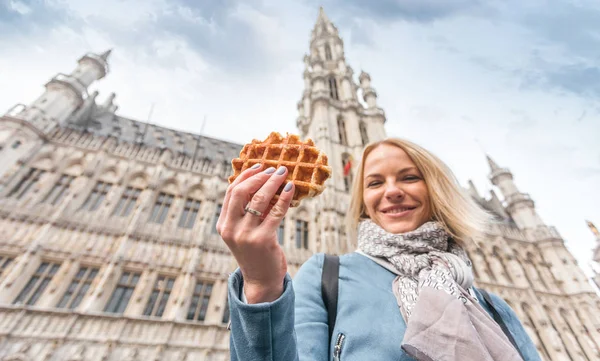 Jovem mulher bonita segurando um waffle belga tradicional no fundo da Grande Praça do Mercado em Bruxelas, Bélgica — Fotografia de Stock