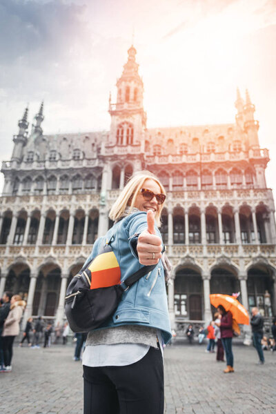 A female traveler stands on Grand Place Square in Brussels and shows her thumbs up, Belgium.